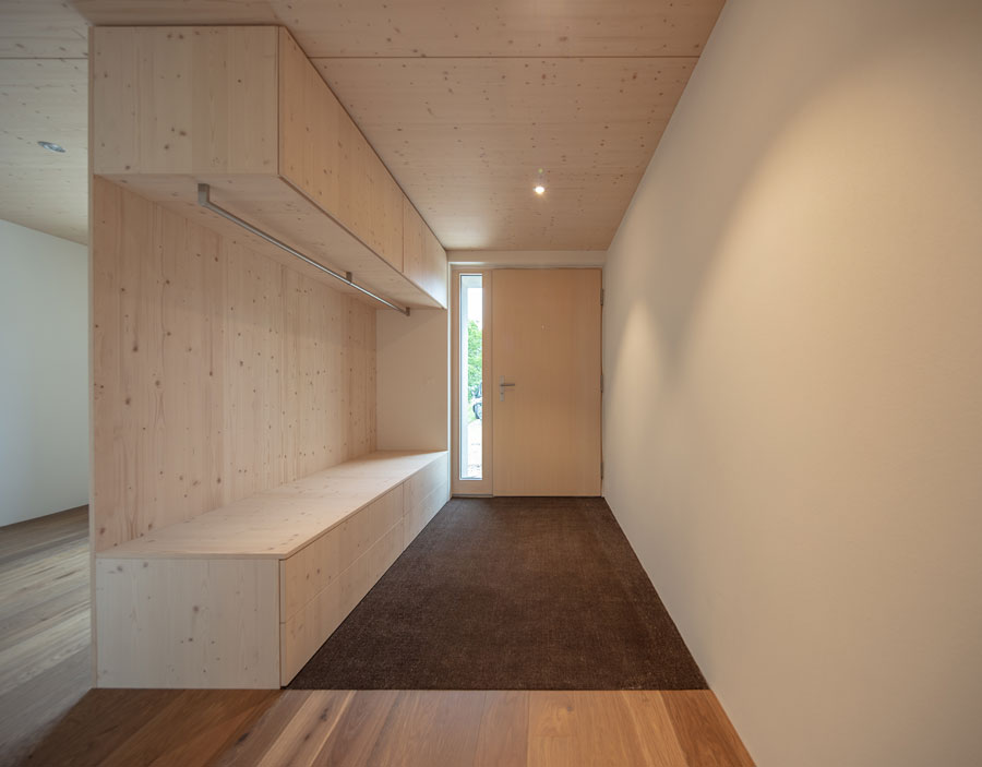 Der neue Eingangssituation in den Mauern des bestehenden Untergeschosses. Neue Oberflächen und ein neues Garderobenmöbel aus Holz sichtbar werten den Raum auf.