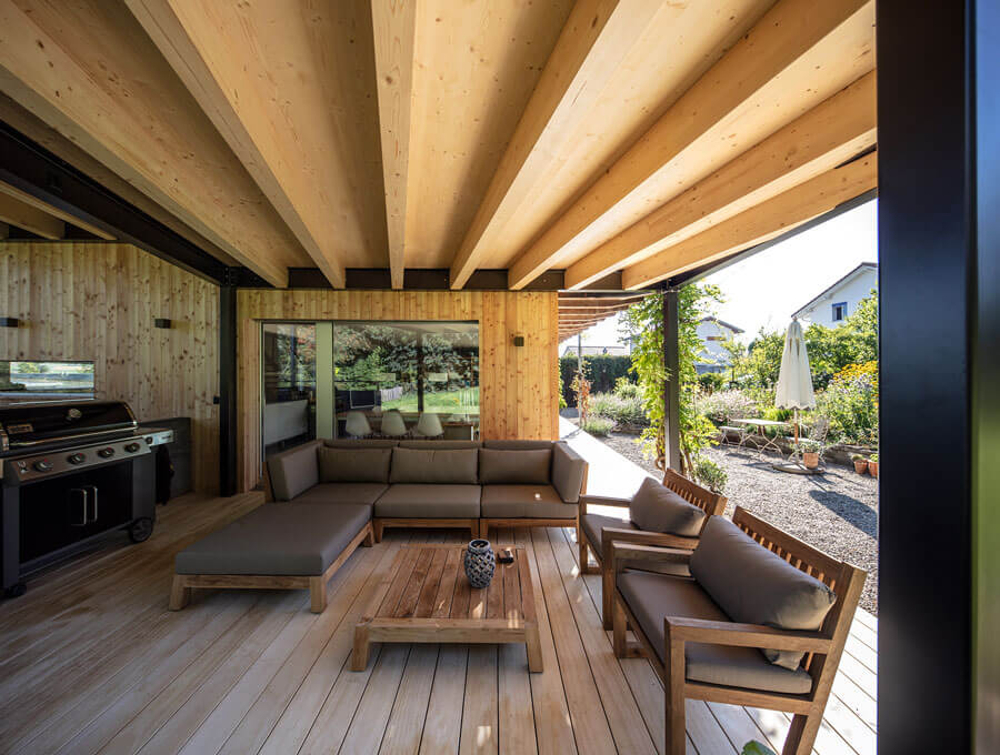 Holzdielen und Holzbalkendecke in Kombination mit schwarzem Stahl laden auf der Terrasse zum entspannen ein.