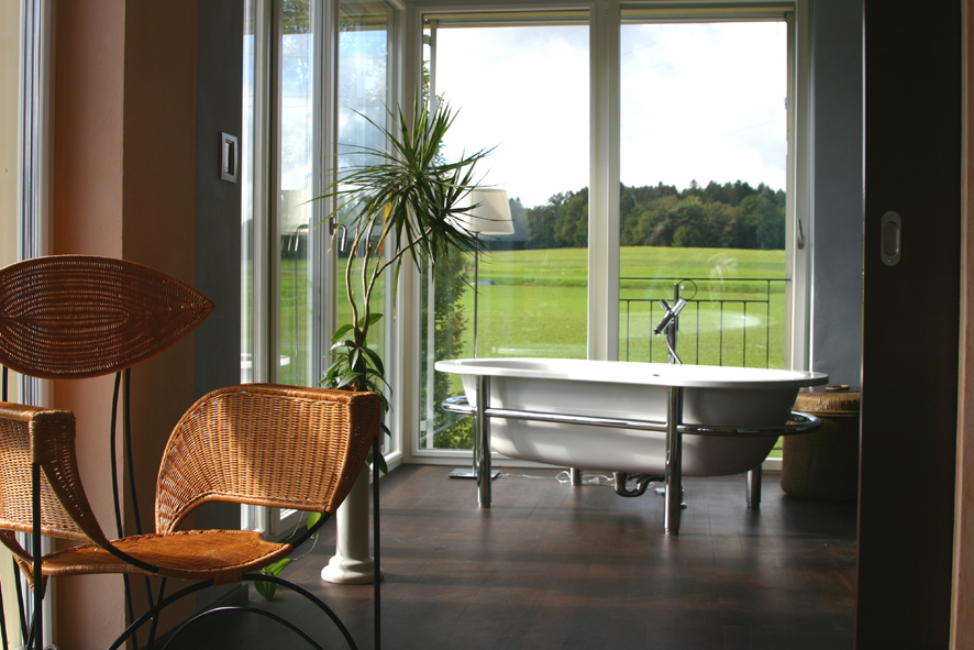 Eine freistehende Badewanne vor einem Eckfenster mit Aussicht ins Grüne-